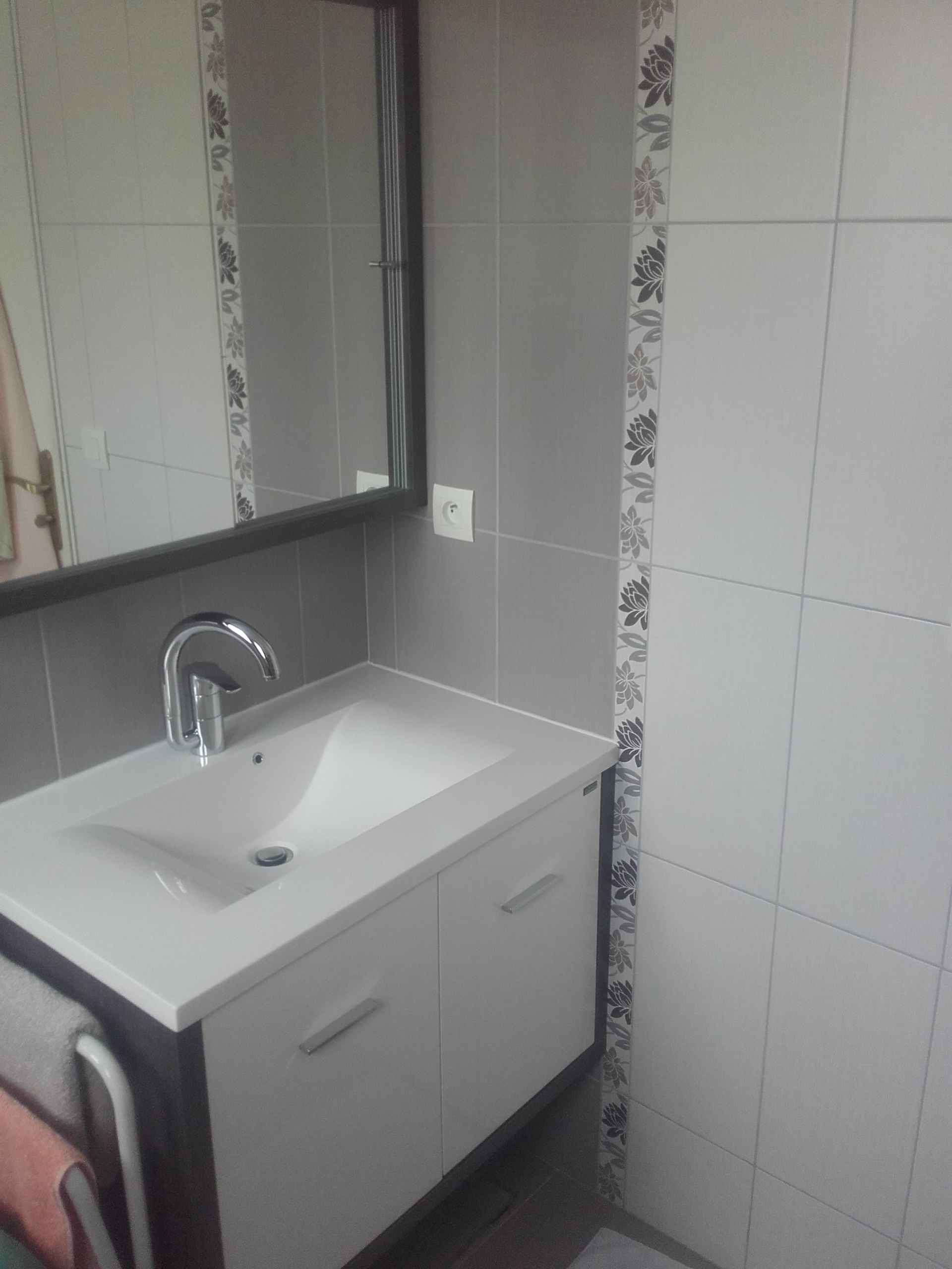 Petit meuble-lavabo de salle de bain avec lavabo blanc, robinet chromé et miroir à côté d'un mur carrelé.