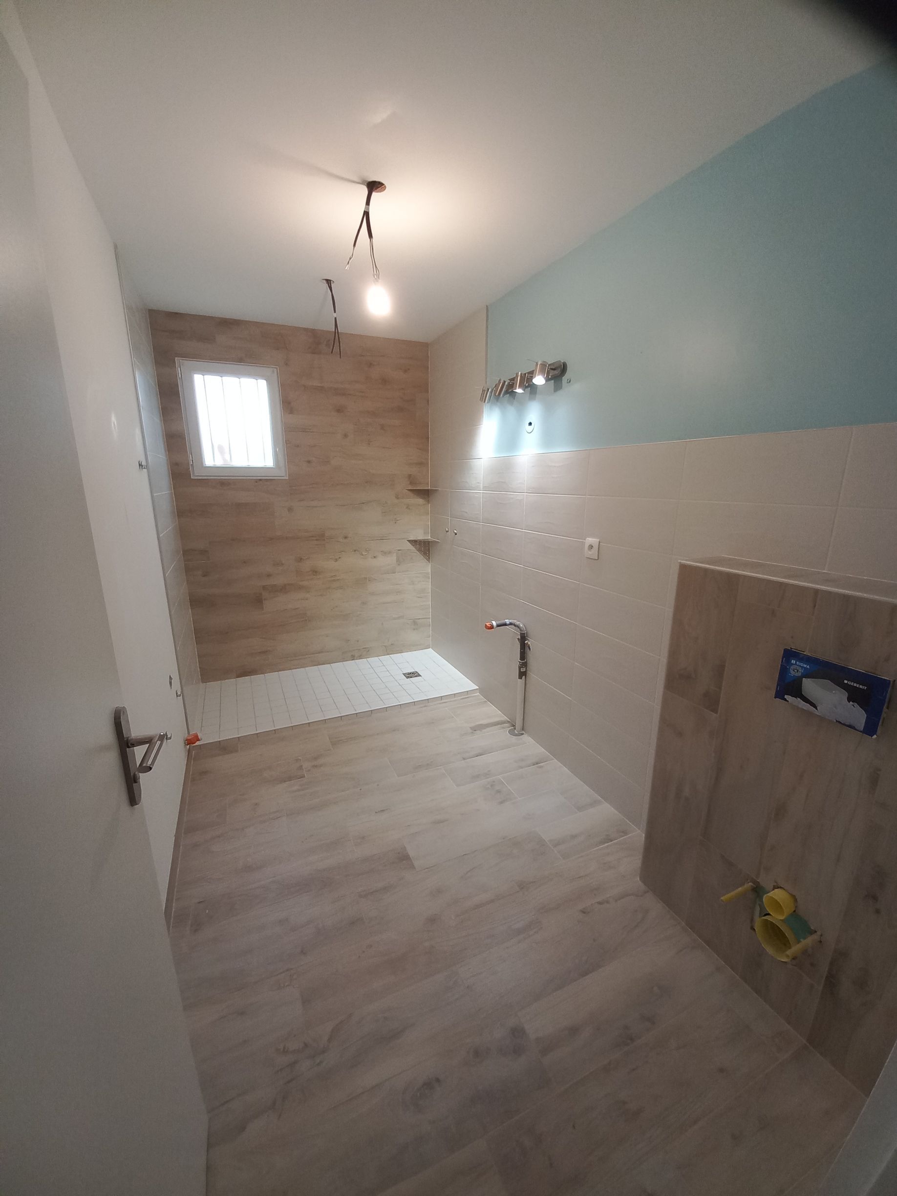 Salle de bains partiellement rénovée avec douche carrelée, parquet clair et meuble vasque sur la droite.