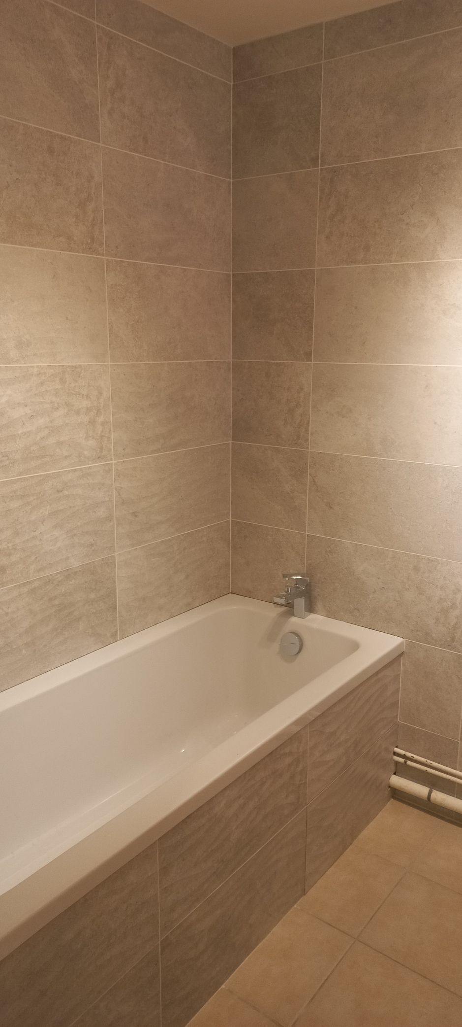 Petite salle de bains carrelée de beige avec baignoire blanche et robinet chromé.