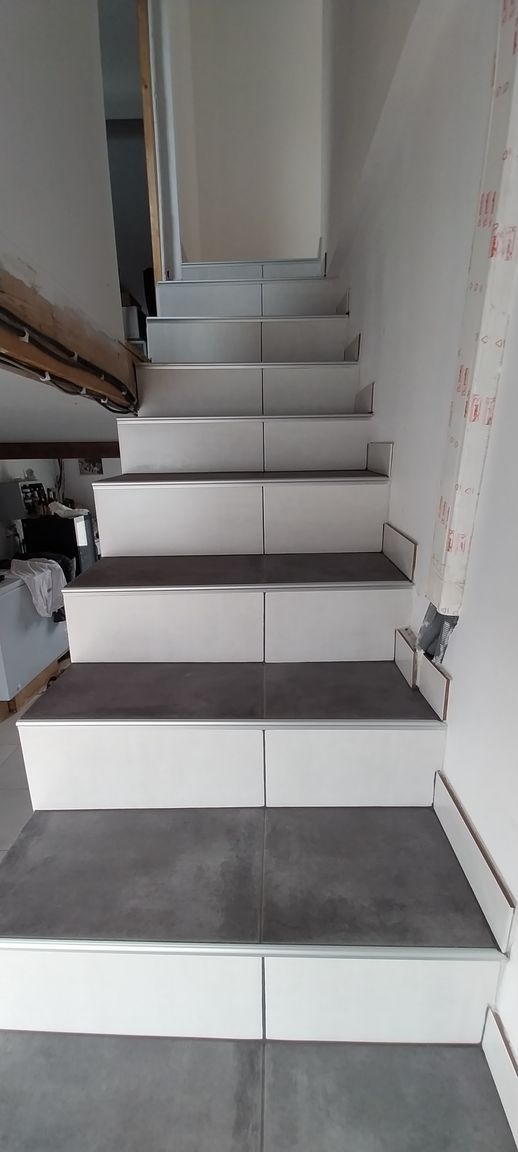 Escalier intérieur étroit aux marches carrelées de blanc menant vers le haut dans un couloir inachevé