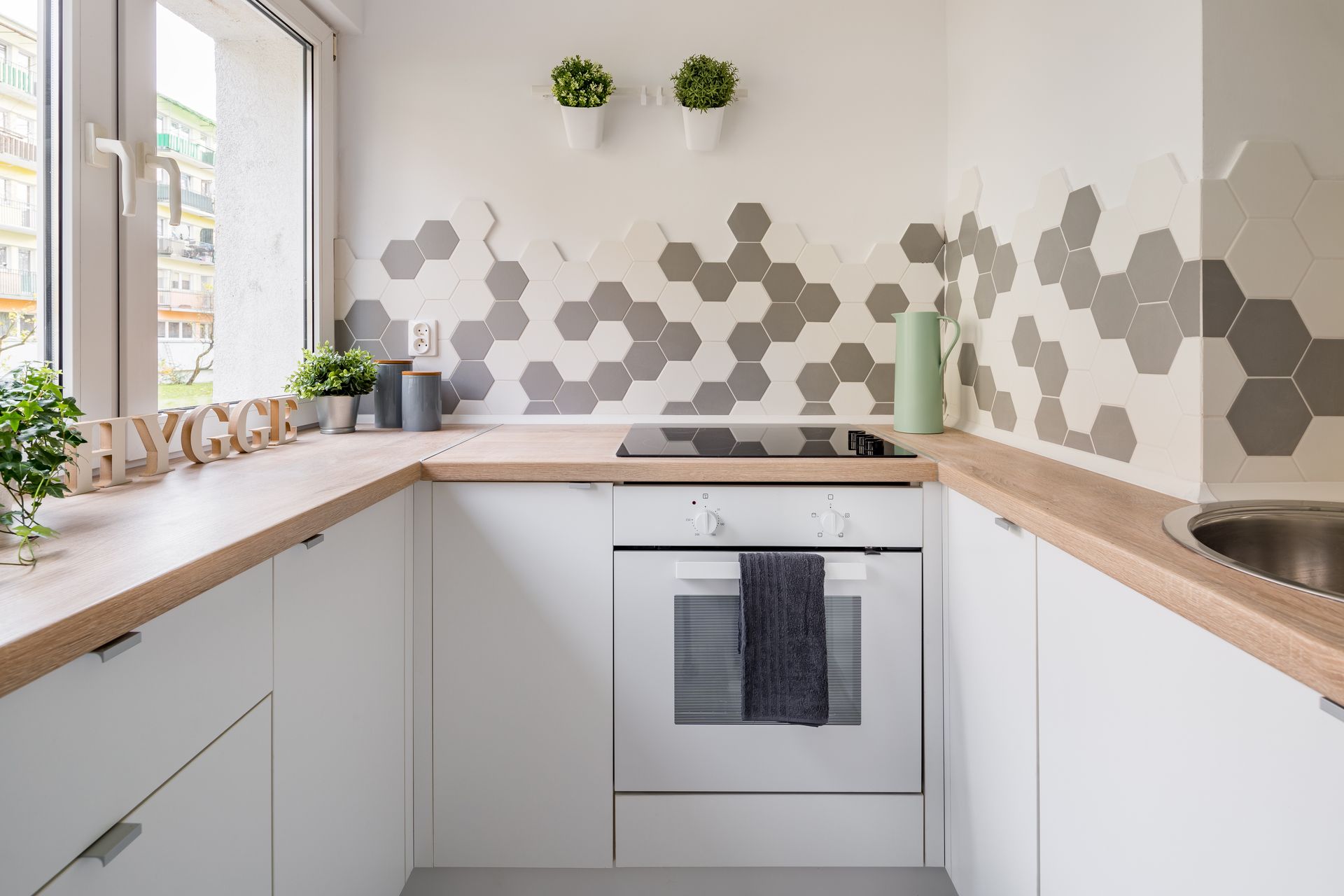 Cuisine moderne blanche avec comptoirs en bois, crédence en carreaux hexagonaux et four encastré