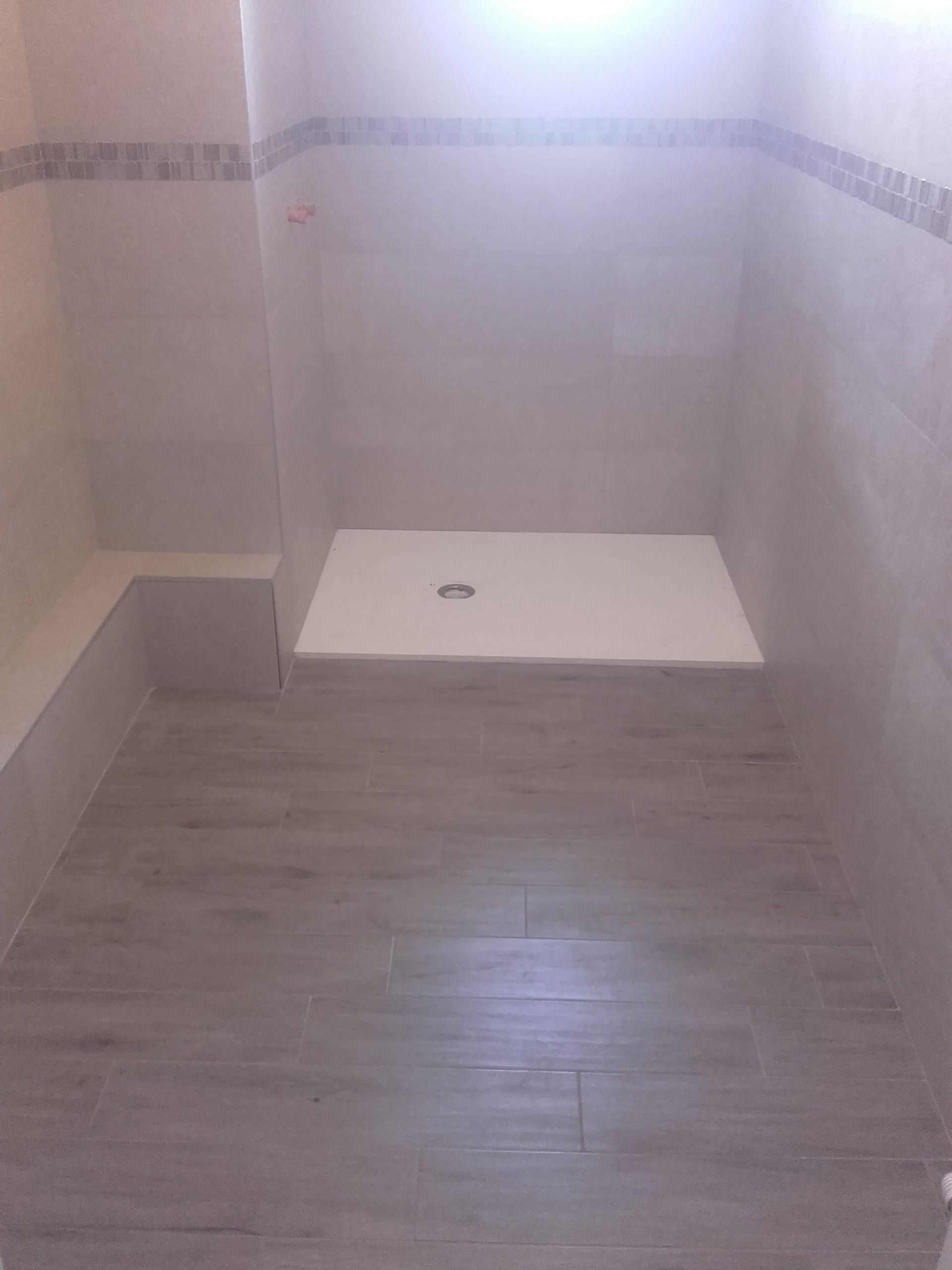 Cabine de douche carrelée vide, avec receveur blanc et murs gris clair.