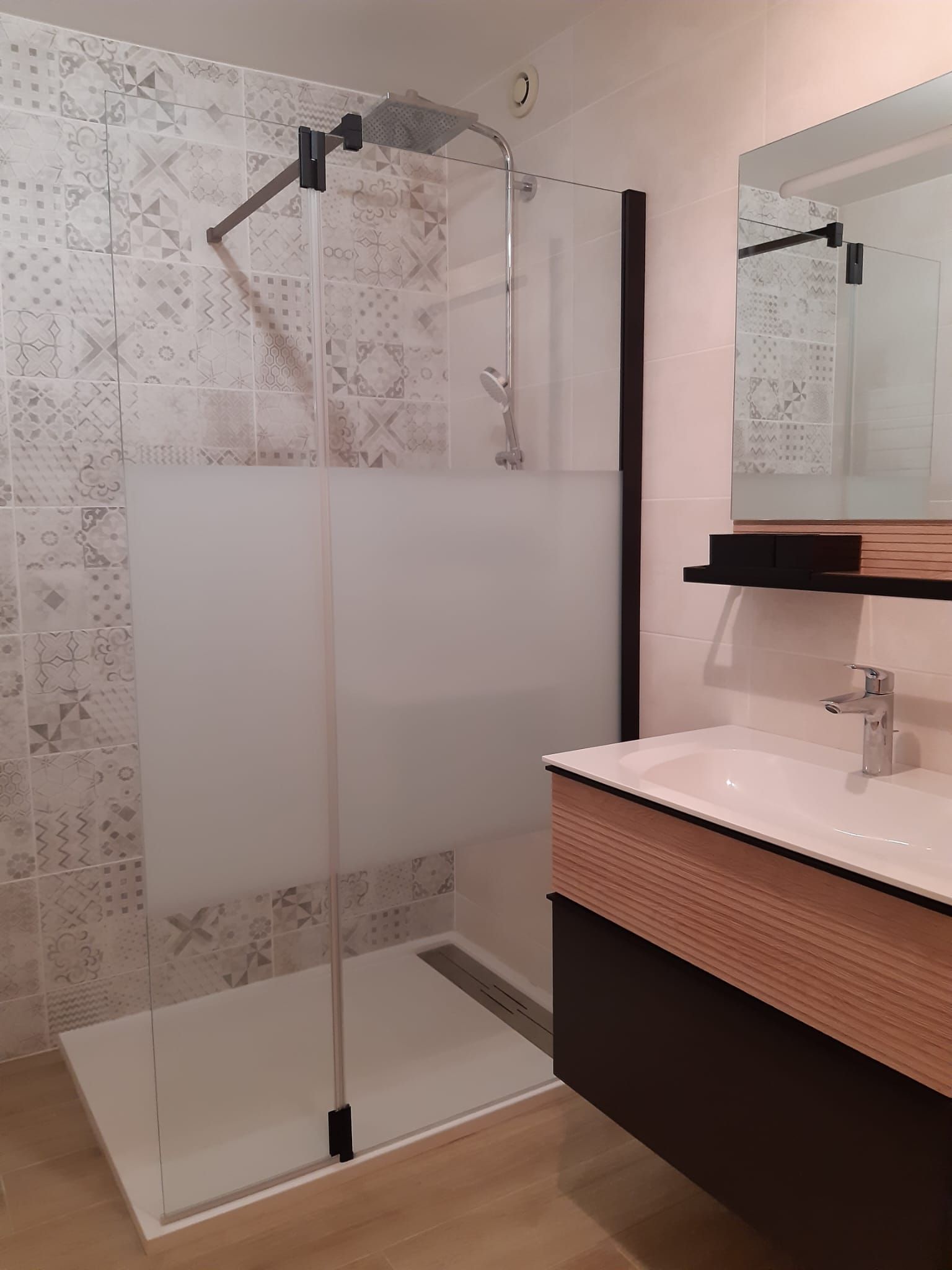 Salle de bains moderne avec paroi de douche en verre, carrelage en mosaïque blanche et meuble-lavabo avec miroir et lavabo.