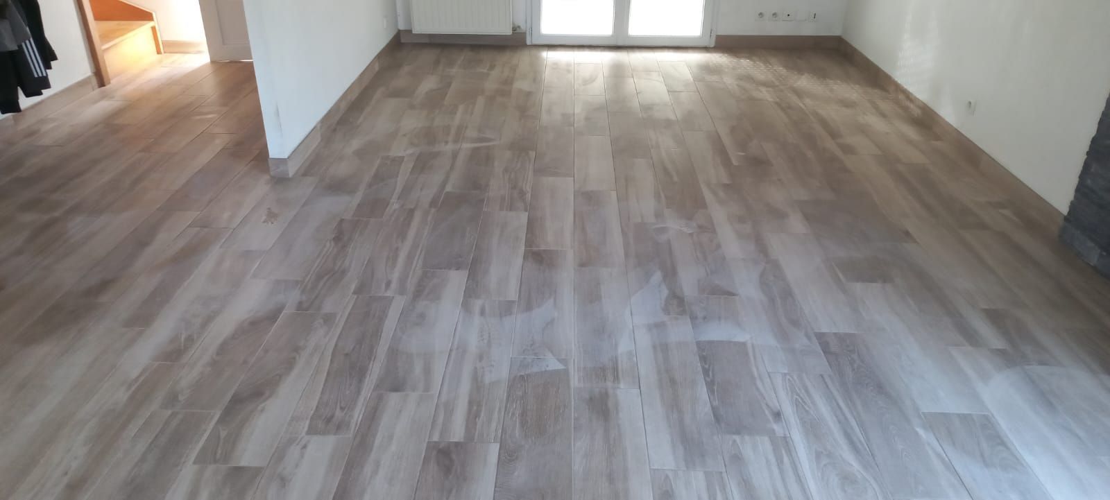 Pièce vide avec un sol gris imitation bois et des fenêtres lumineuses au fond.