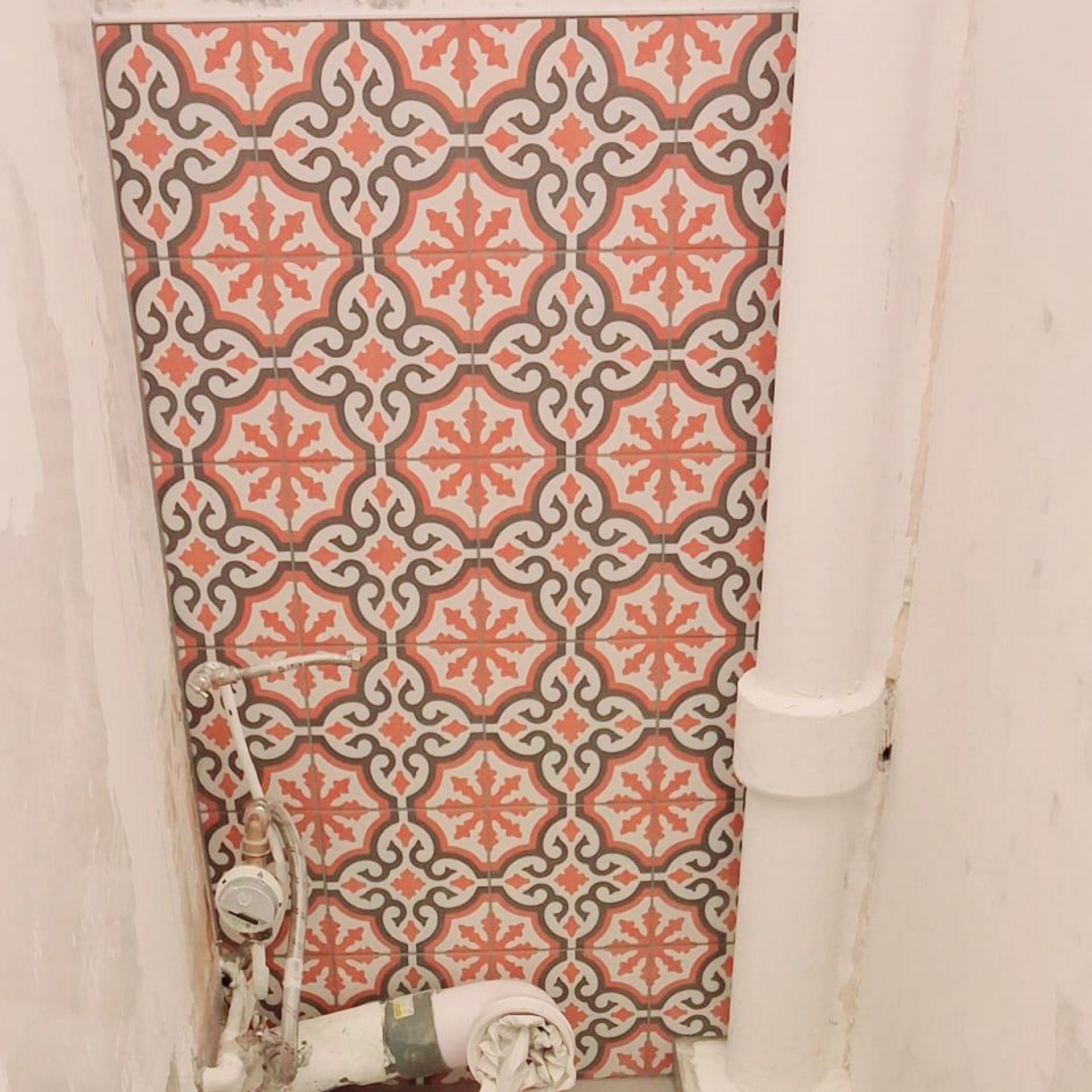 Mur carrelé en carreaux de ciment à côté de tuyaux de plomberie blancs et d'une vanne dans une petite salle de bains.