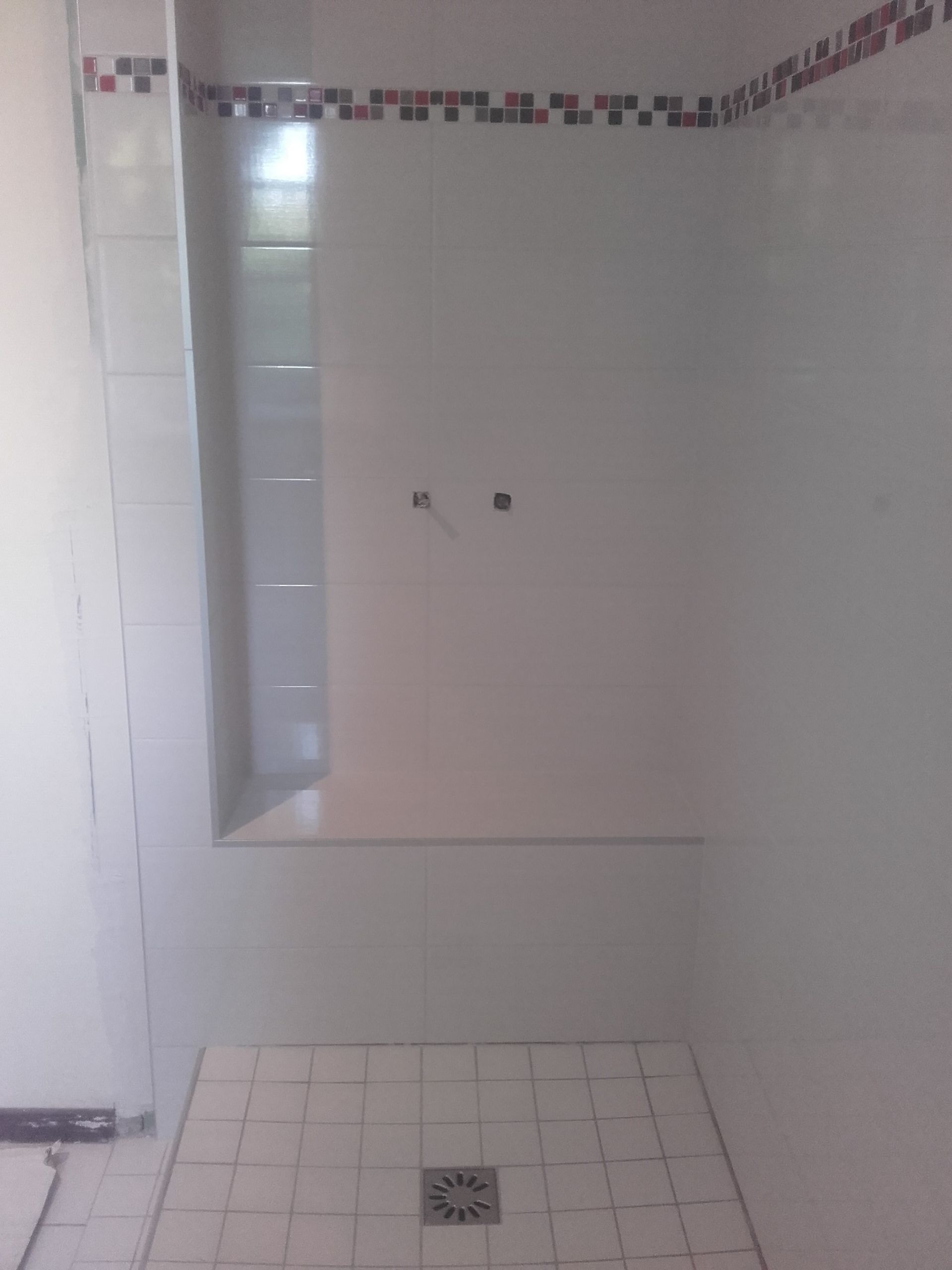 Cabine de douche carrelée vide avec banc intégré et bonde de sol