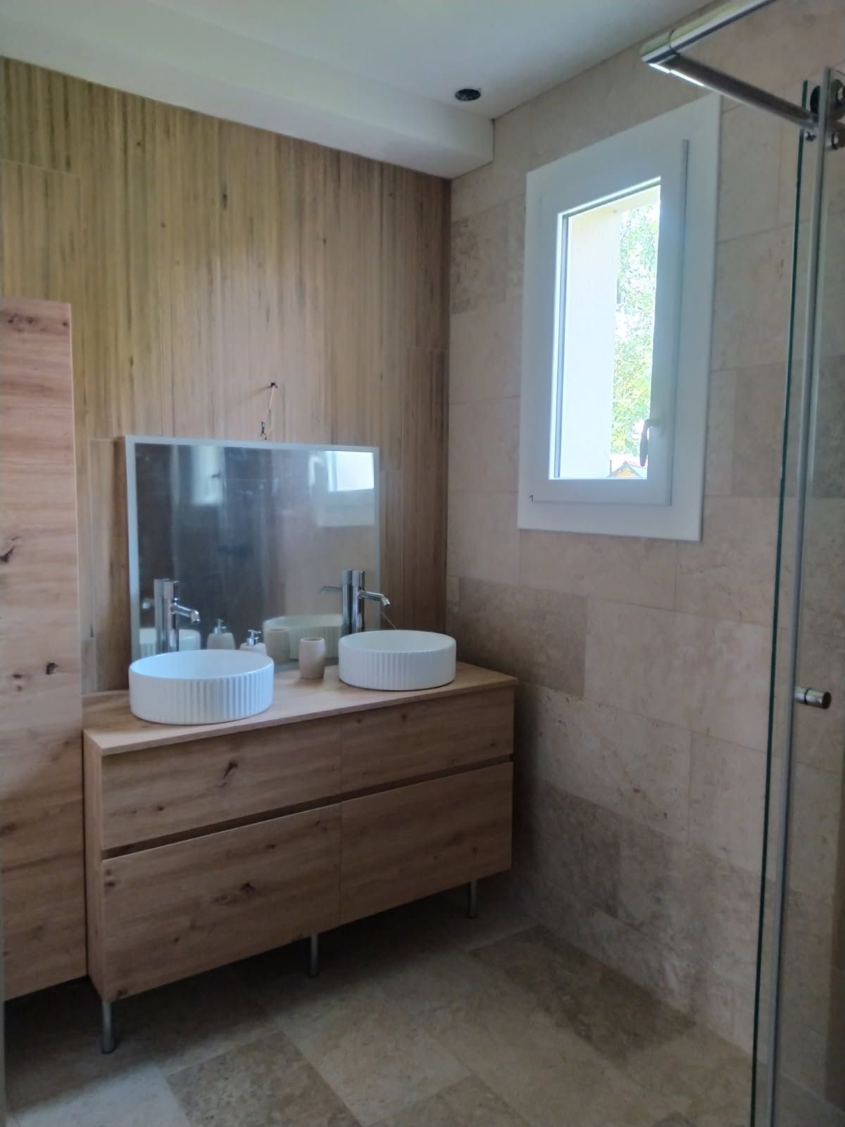 Salle de bains moderne avec meuble lavabo en bois, double vasque, miroir, carrelage beige et petite fenêtre