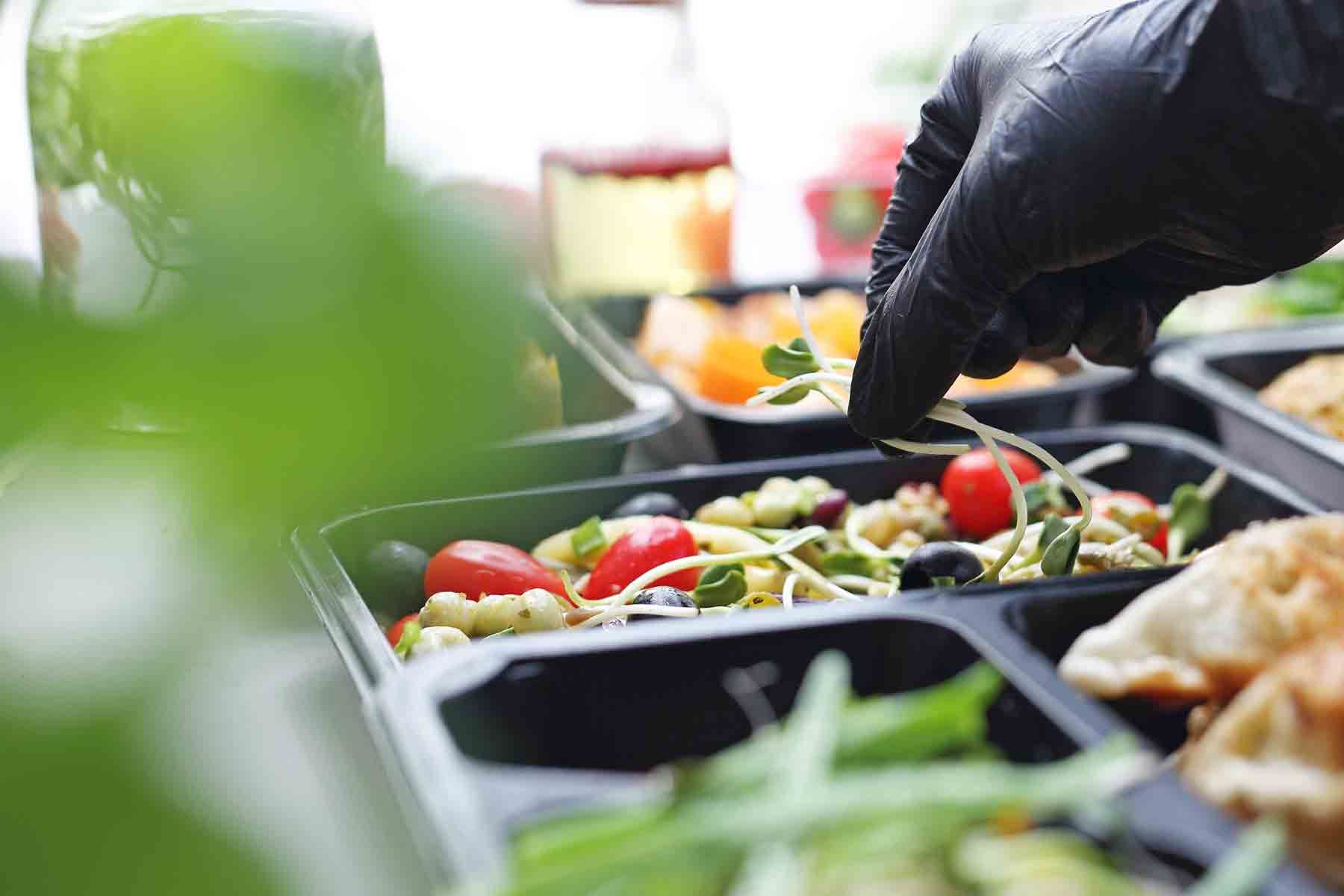Main avec gant noir déposant une plante aromatique dans une plat à emporter
