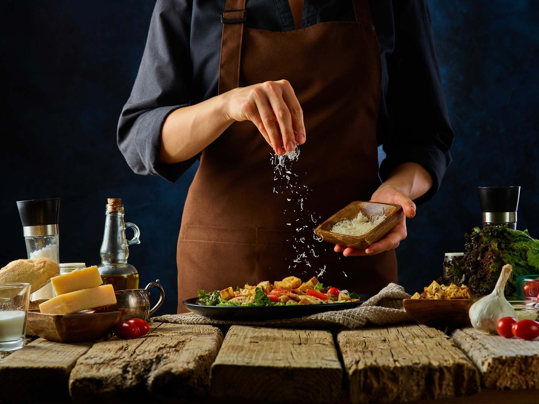 Un cuisinier avec tablier saupoudrant de sel un plat