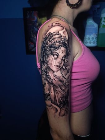 Mujer con un tatuaje de media manga de una mujer mística de ojos blancos y cabello suelto. Lleva una camiseta rosa sin mangas.