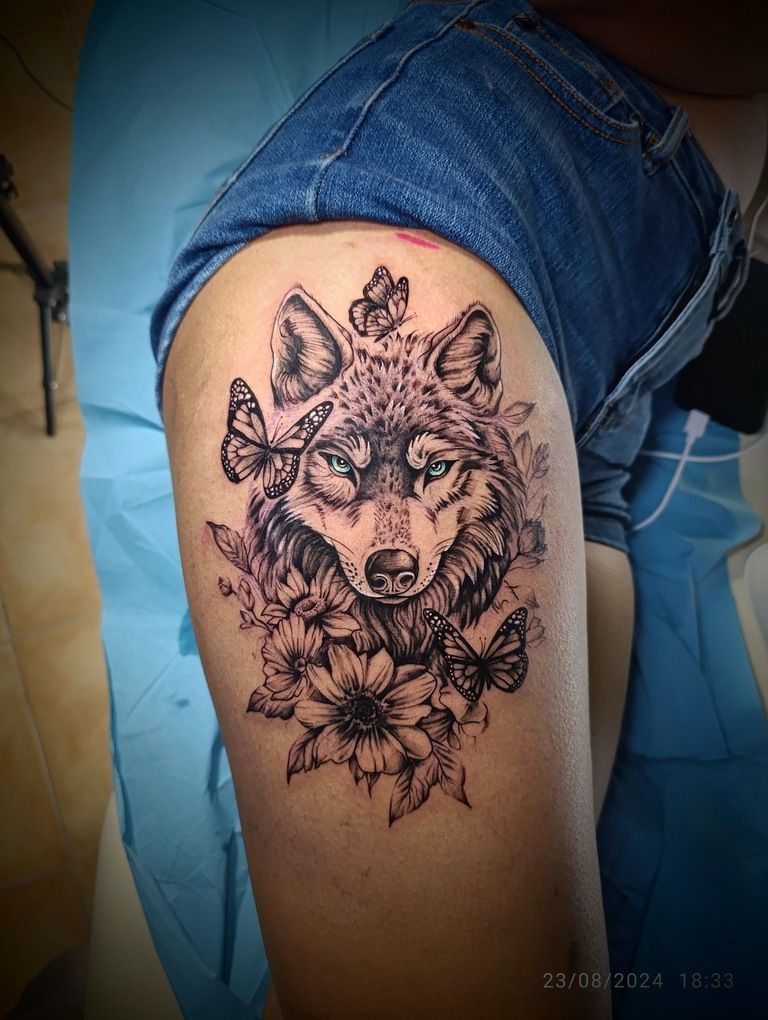 Una mujer tiene un tatuaje de un lobo con flores y mariposas en el muslo.