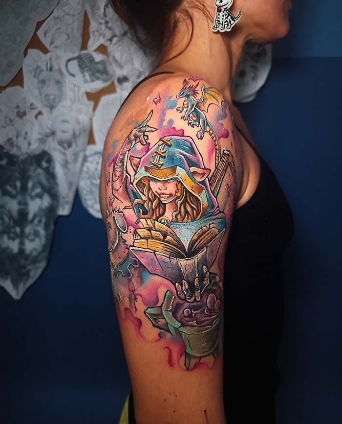 Tatuaje de un mago de fantasía leyendo un libro, con fondo de acuarela colorido en el brazo de una persona.