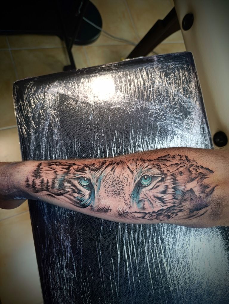 Una persona tiene un tatuaje de ojos de tigre en su antebrazo.