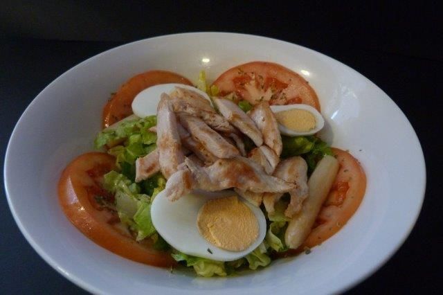 Una ensalada con pollo, huevos, tomates y lechuga en un tazón blanco.