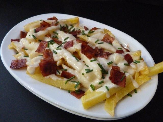 Un plato blanco cubierto con papas fritas, queso y tocino.