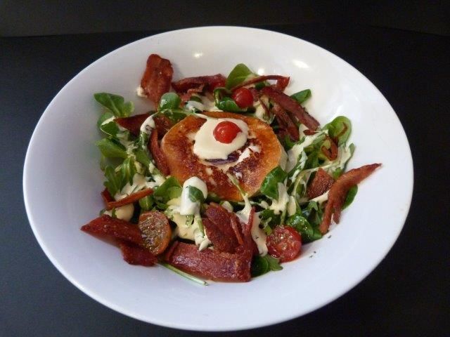 Una ensalada en un tazón blanco con un tomate encima.