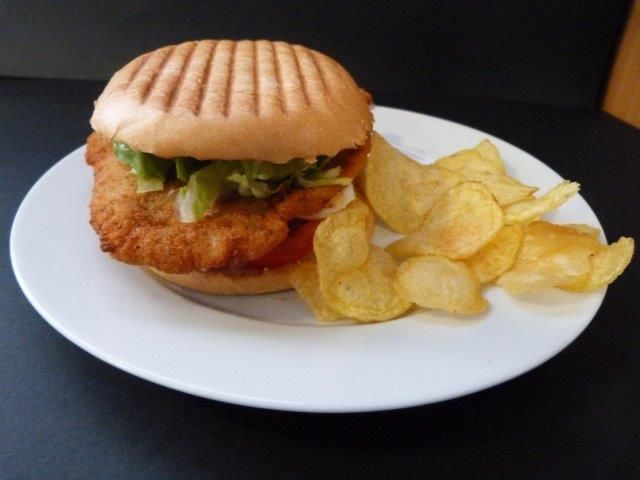 Un plato blanco cubierto con un sándwich de pollo y patatas fritas.
