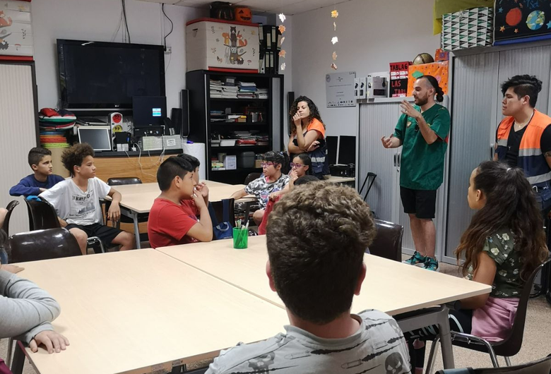 Los niños en el aula escuchan a dos adultos, uno de los cuales habla.