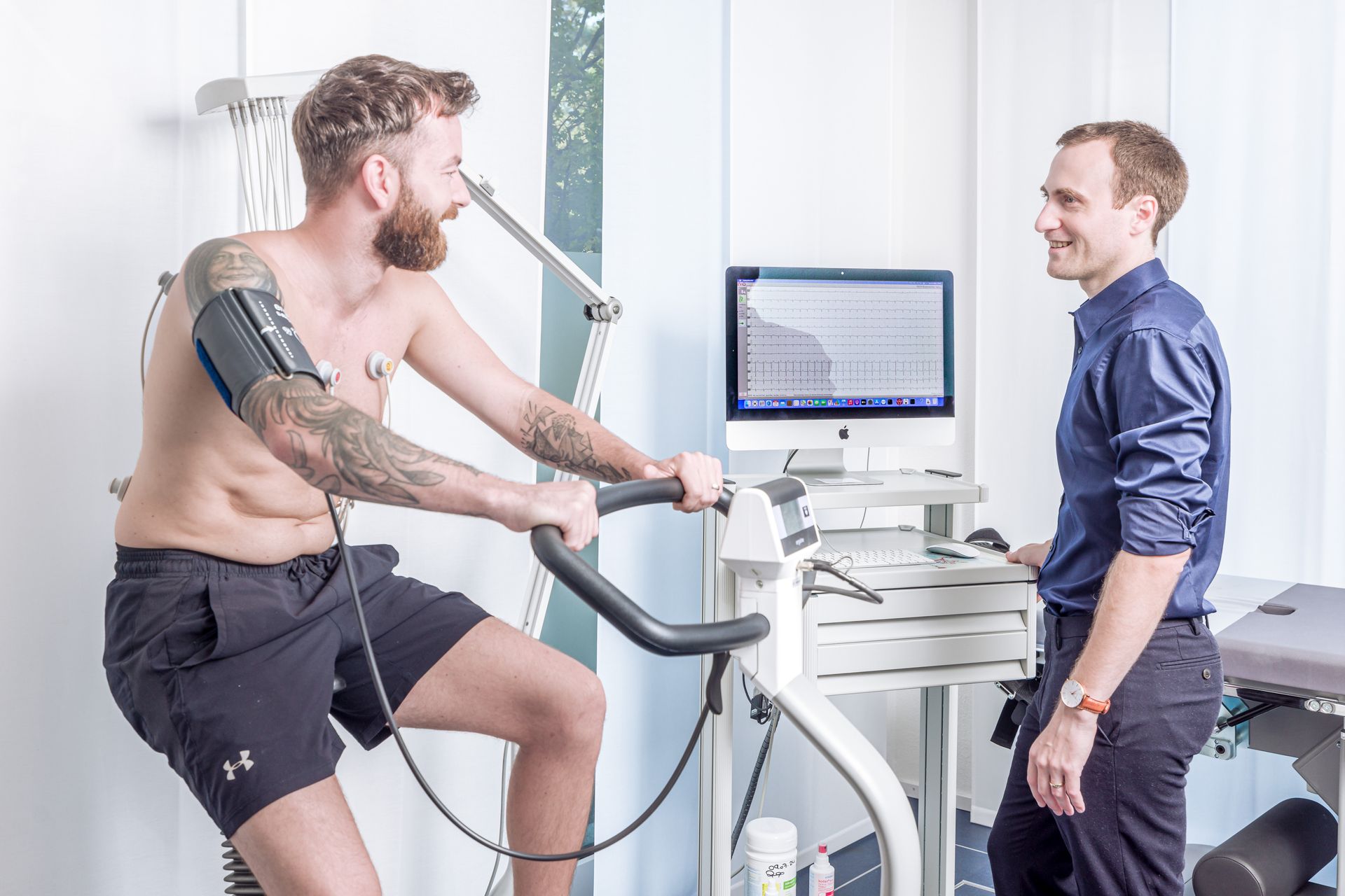 Ein Mann fährt auf einem Heimtrainer, während ein Arzt zusieht.