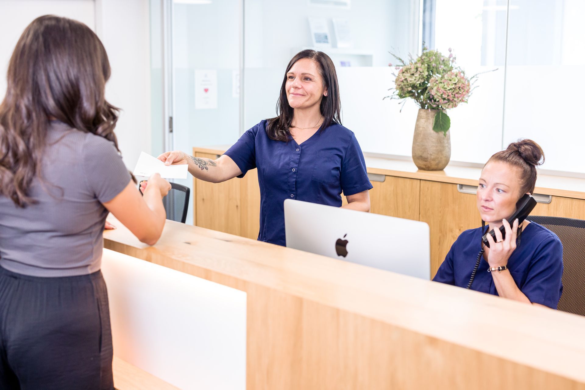 Eine Frau steht an einem Rezeptionstresen und telefoniert mit einem Mobiltelefon.