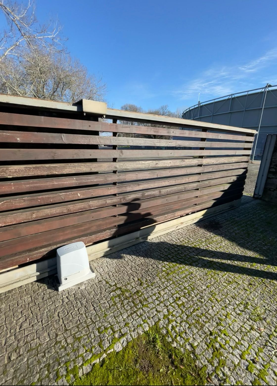A wooden fence with a sliding gate is sitting on a cobblestone driveway.
