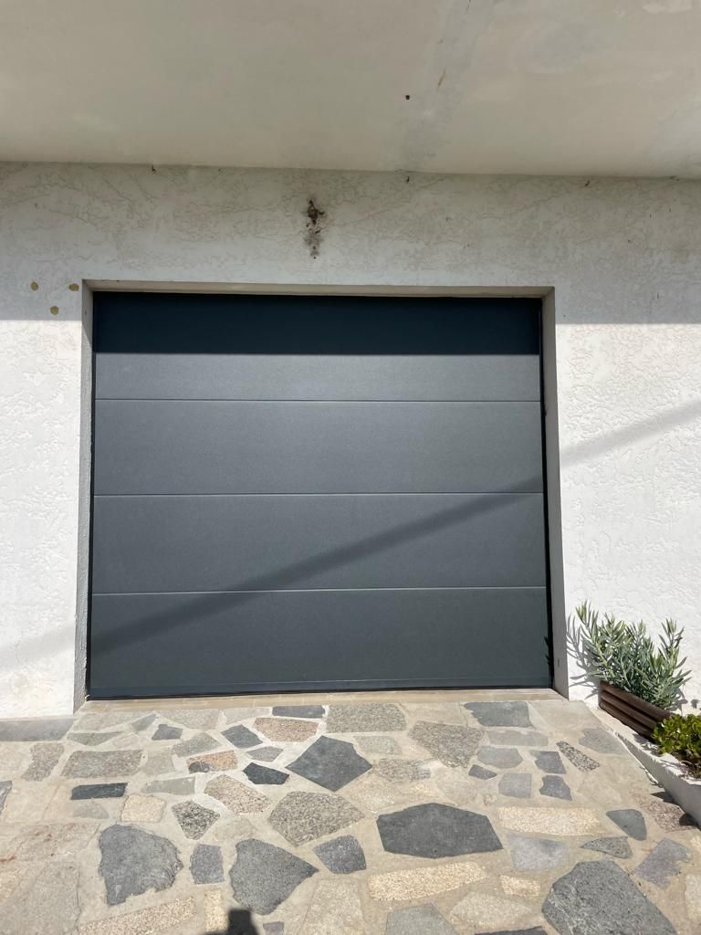 A gray garage door is sitting on top of a stone driveway.