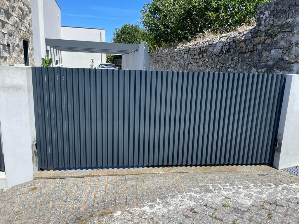 A black sliding gate is sitting in front of a stone wall.