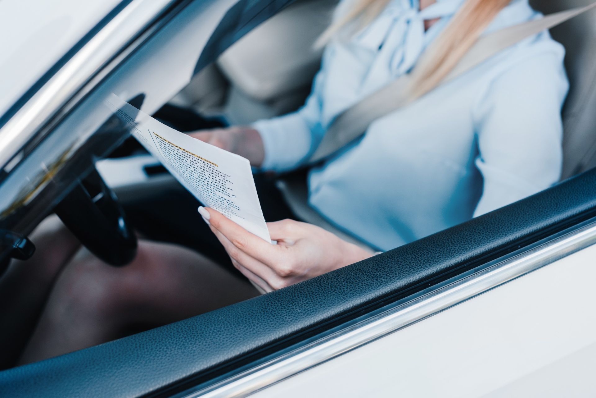 Una mujer está sentada en un coche leyendo un trozo de papel.
