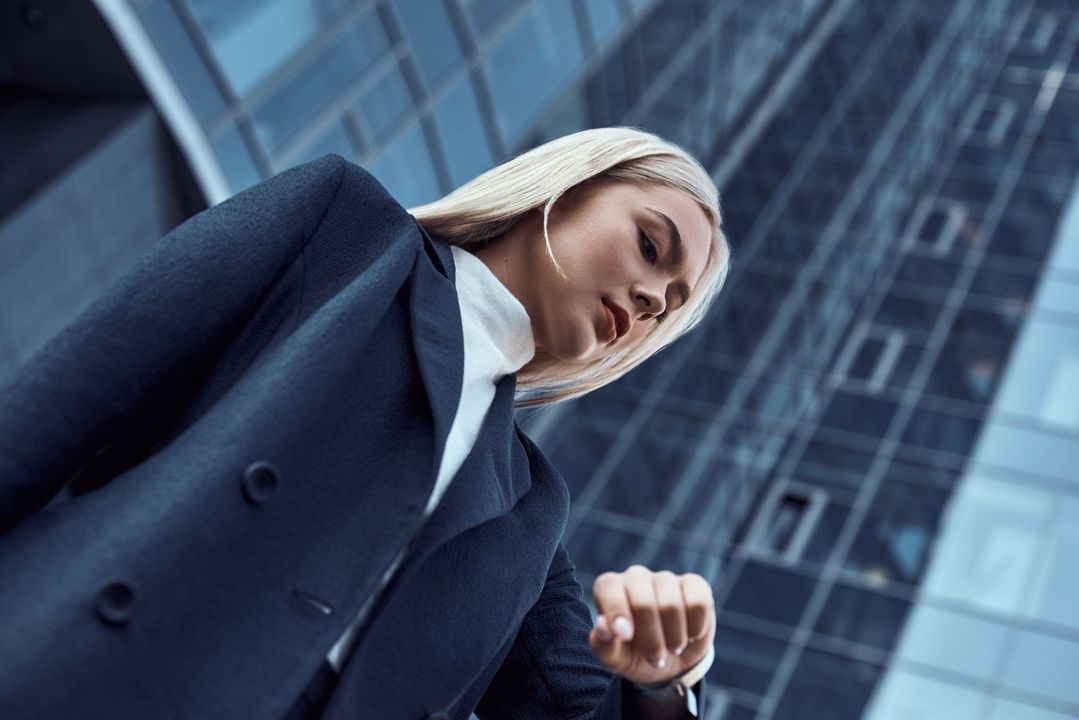 Una mujer con traje está parada frente a un edificio alto mirando su reloj.