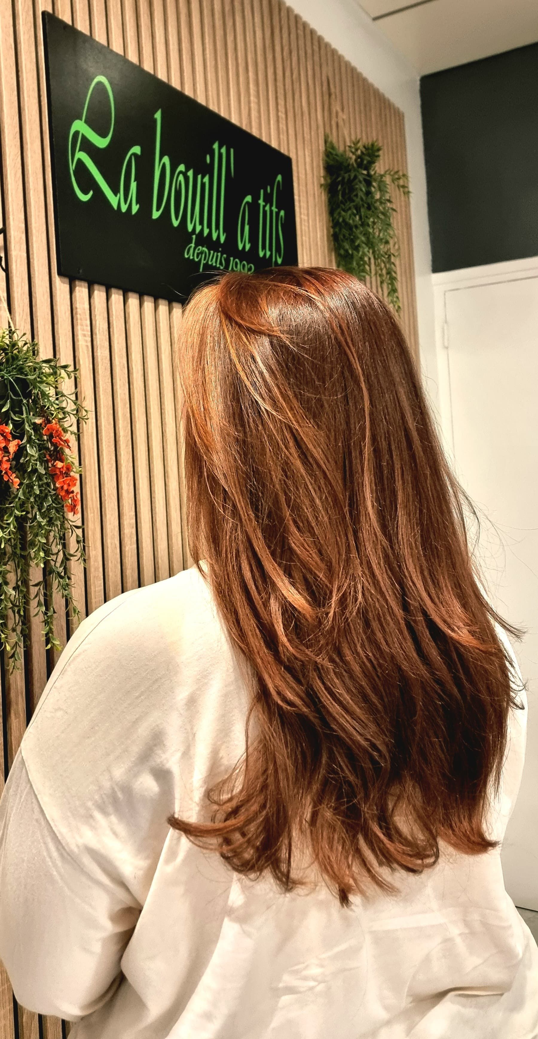 Femme aux longs cheveux bruns face à une enseigne verte de salon dans un intérieur lumineux