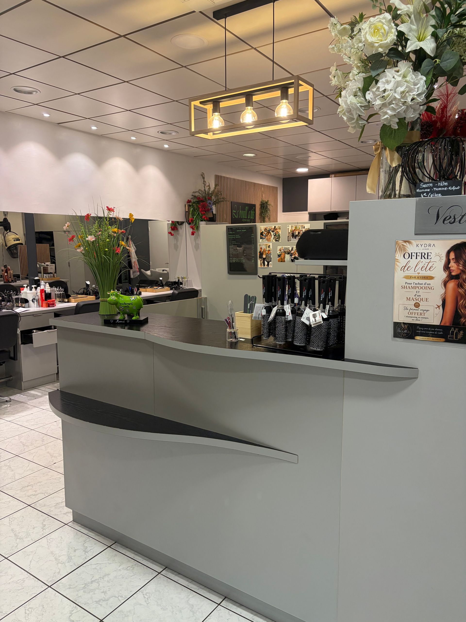 Comptoir d'accueil moderne pour salon de coiffure, agrémenté de fleurs, de miroirs et d'un éclairage doux au plafond, dans un intérieur lumineux.