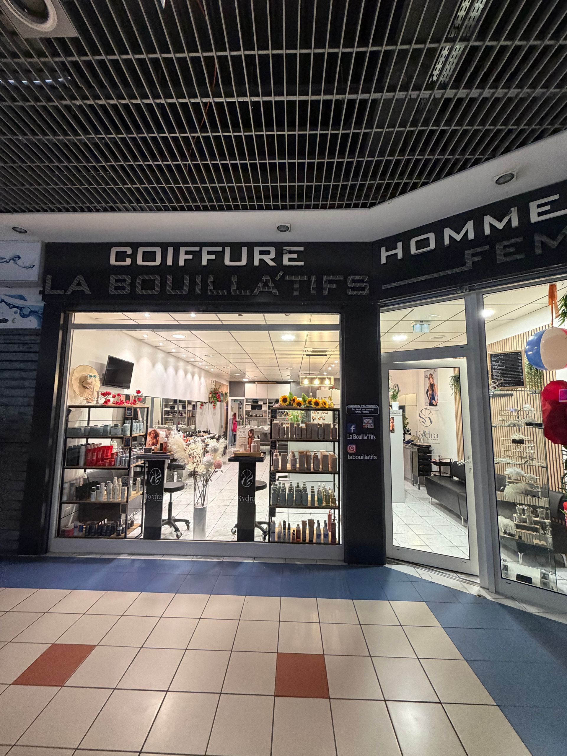 Façade d'un salon de coiffure et d'un magasin de vêtements pour hommes avec vitrines éclairées dans un centre commercial couvert