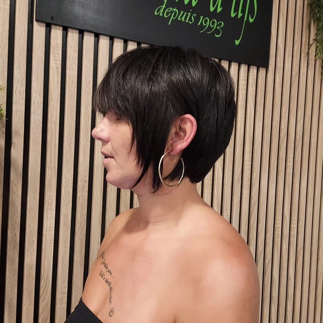 Portrait de profil d'une personne aux cheveux noirs courts et portant des boucles d'oreilles créoles, sur fond rayé.