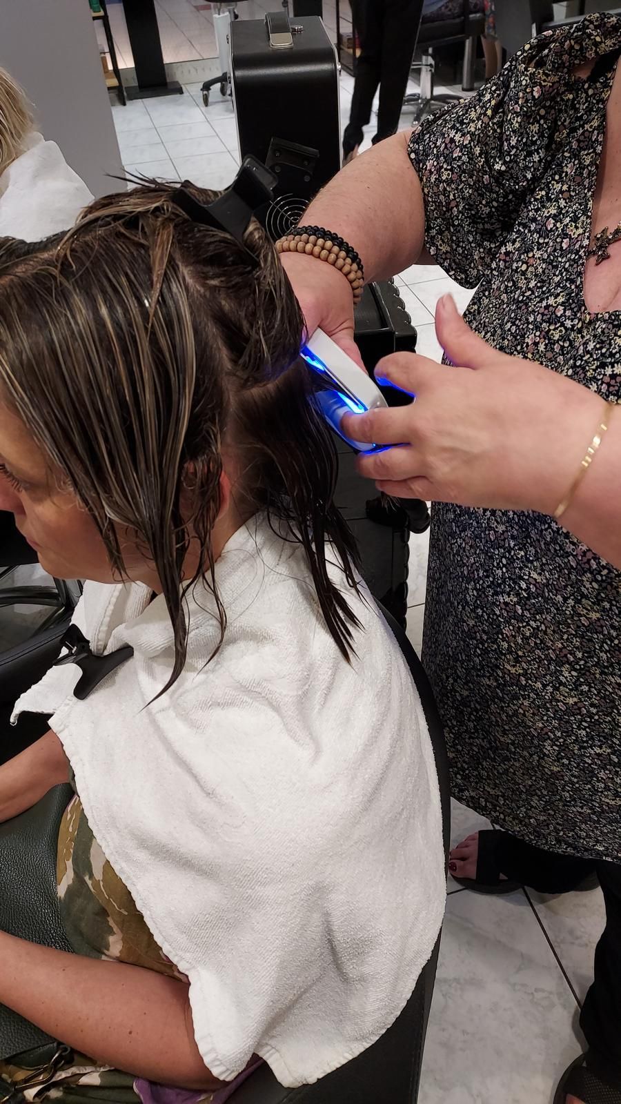 Coiffeuse utilisant une tondeuse à lumière bleue pour couper les cheveux mouillés d'une cliente assise dans un salon