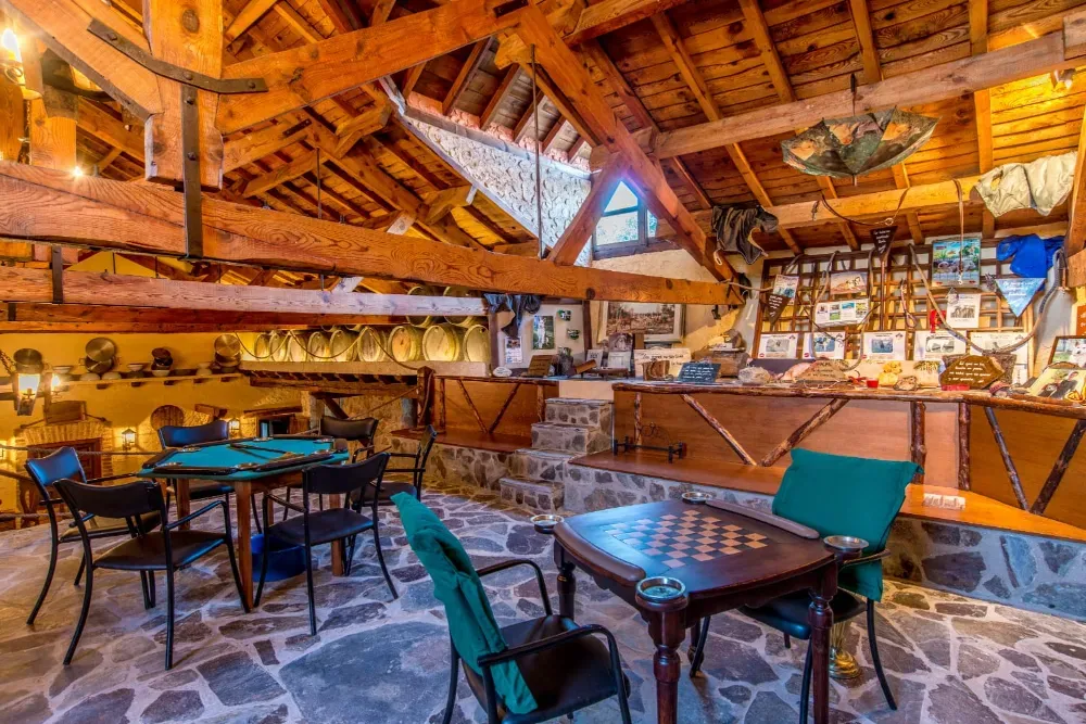 Sala de juegos rústica con vigas de madera, suelos de piedra, mesas de juego con tableros verdes y una colección de adornos de pared.