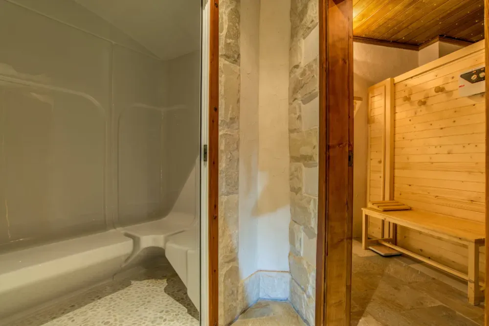 Una bañera blanca y una cabina de ducha junto a una sauna de madera abierta con bancos de madera integrados.