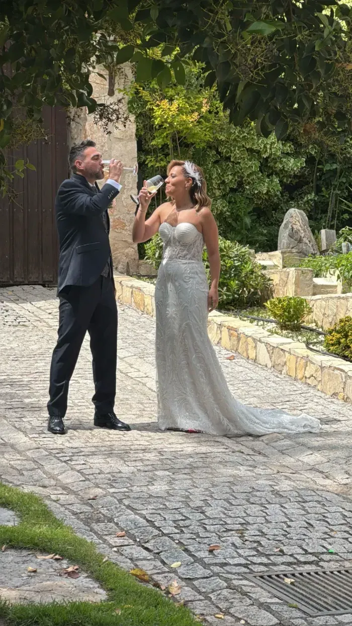 Una pareja vestida de boda se encuentra en un sendero de piedra, alzando sus copas en un brindis de celebración al aire libre.