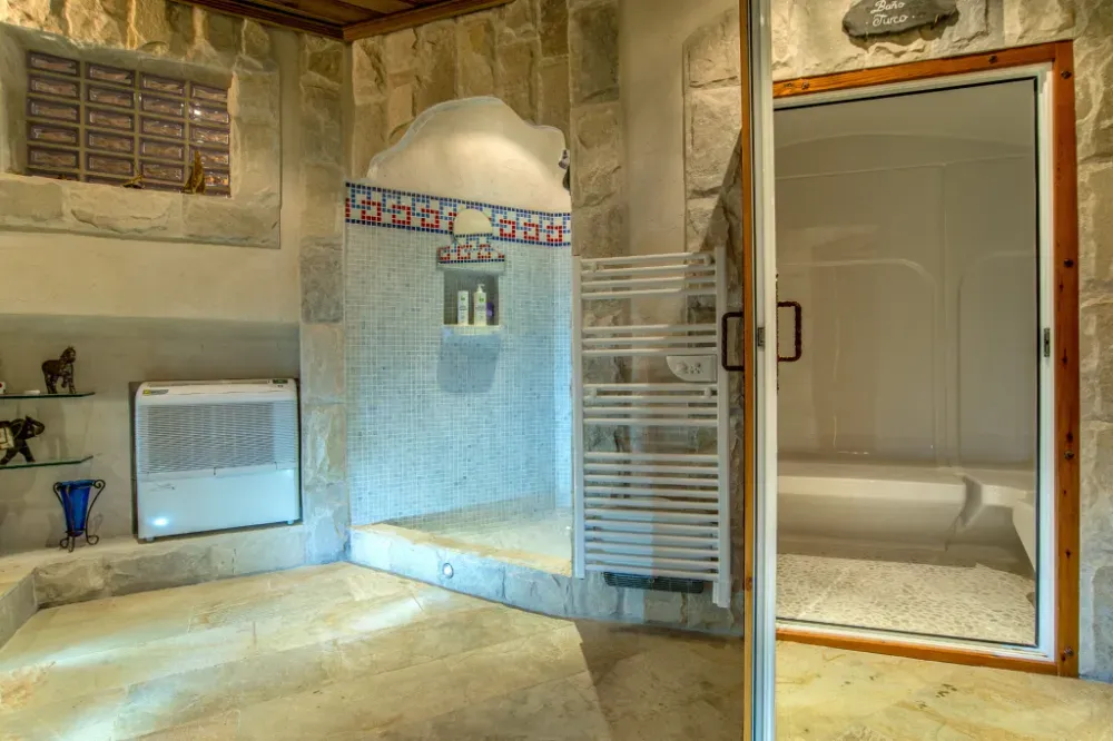 Un baño con paredes de piedra que cuenta con una ducha a ras de suelo con una pared de azulejos de mosaico y una cabina de ducha independiente con mampara de cristal.