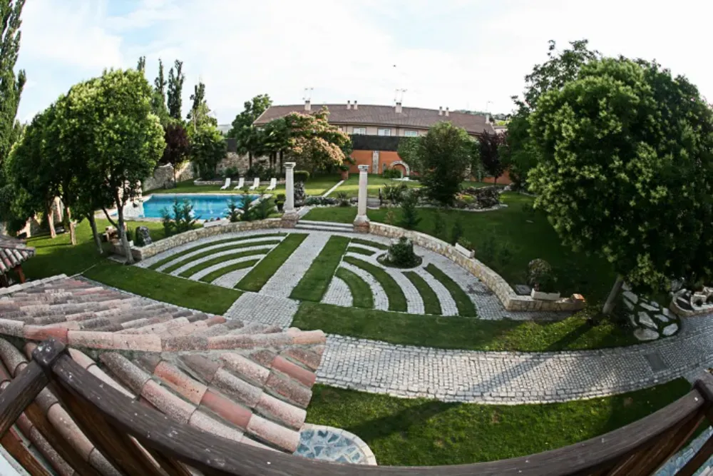 Vista panorámica de un patio trasero con un jardín semicircular con senderos de piedra, una piscina y una casa.
