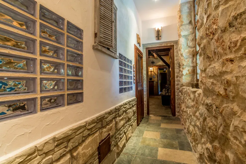 Un pasillo con una pared de piedra a la derecha, una pared blanca con ventanas de bloques de vidrio a la izquierda y una puerta de madera al frente.