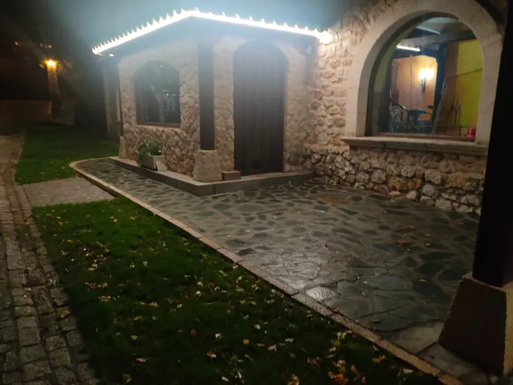 Vista exterior de un edificio de piedra por la noche, con un patio pavimentado, una ventana arqueada y una iluminación cálida en el techo.
