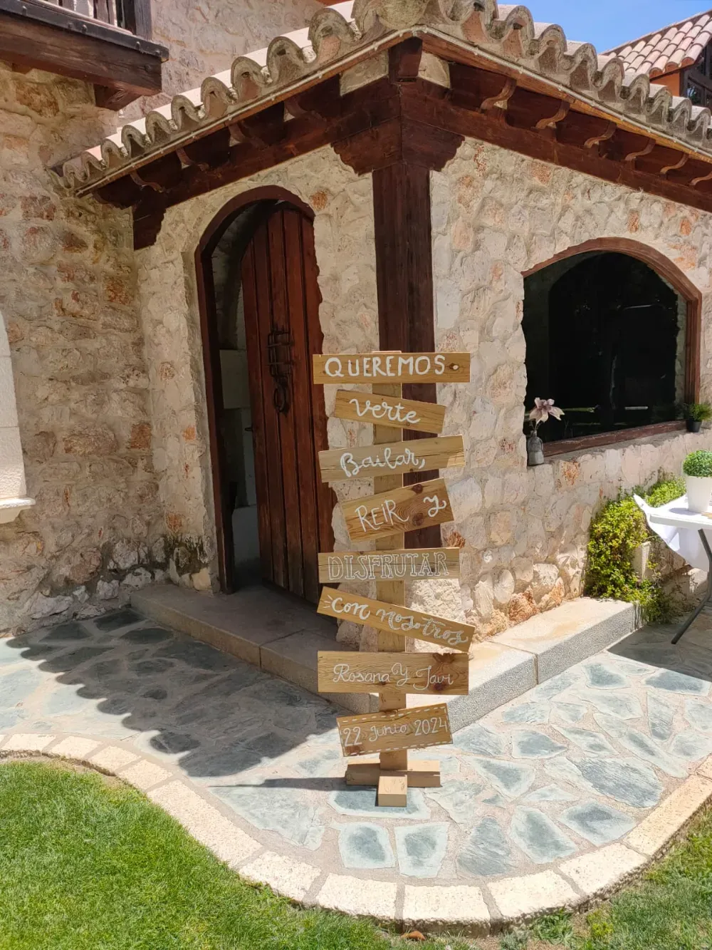 Un poste indicador de madera con flechas direccionales se alza frente a un edificio rústico de piedra en un recinto al aire libre.