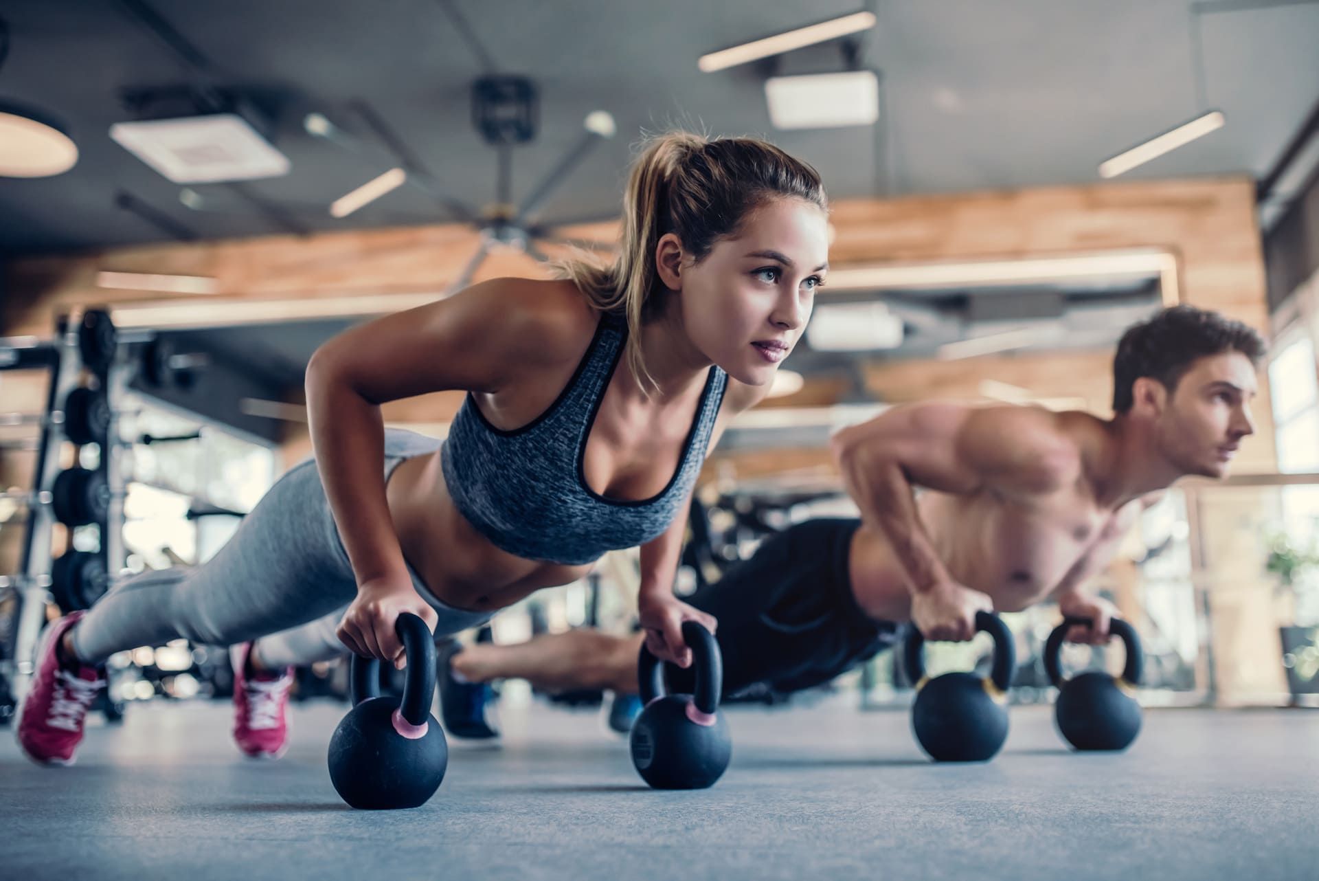 Ein Mann und eine Frau machen Push-ups mit Gewichten in einem Fitnessstudio | bodyfit24