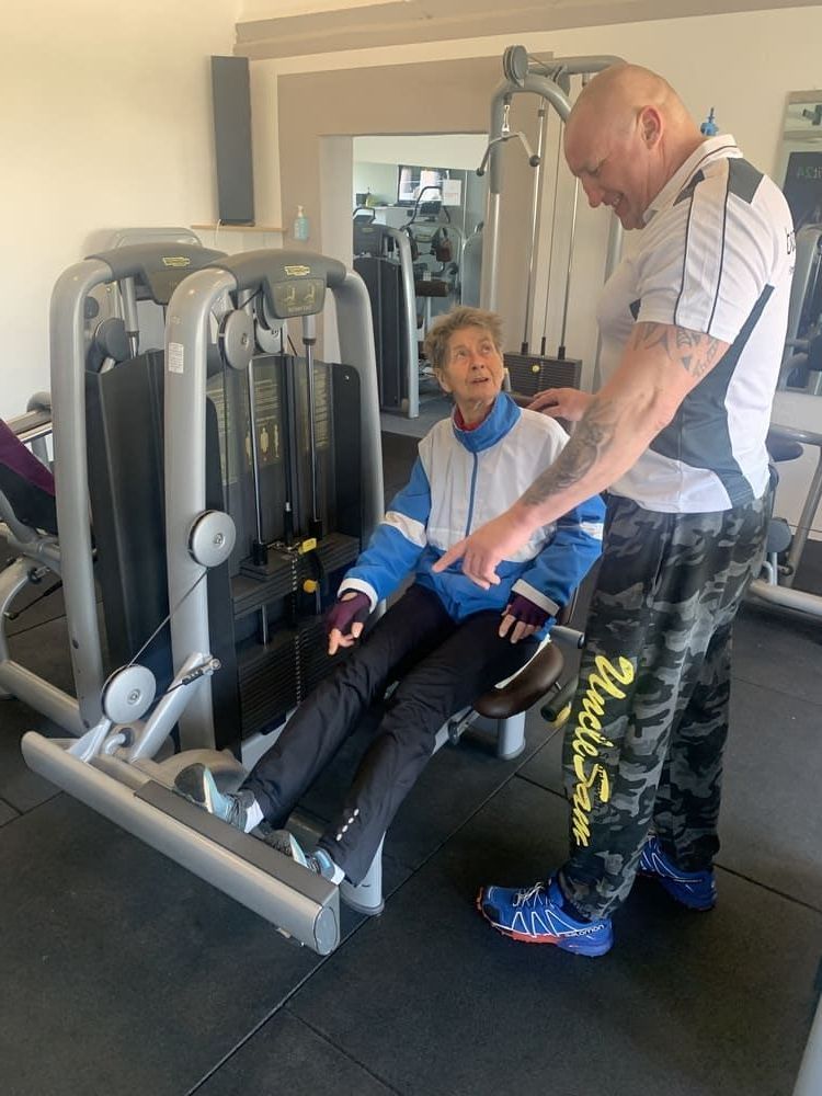 Ein Mann hilft einer älteren Frau in einem Fitnessstudio | bodyfit24