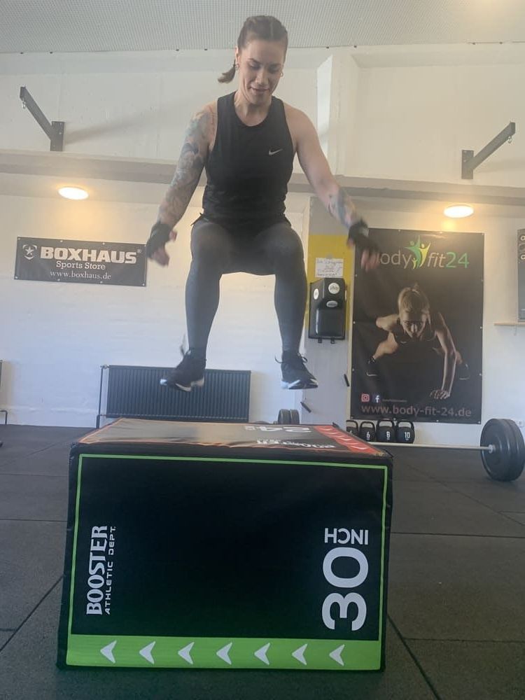 Eine Frau springt auf einer Box in einem Fitnessstudio | bodyfit24