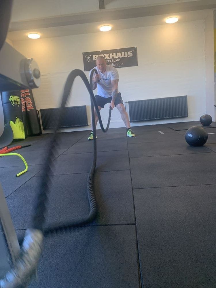 Ein Mann spielt mit einem Kampfseil in einem Fitnessstudio | bodyfit24