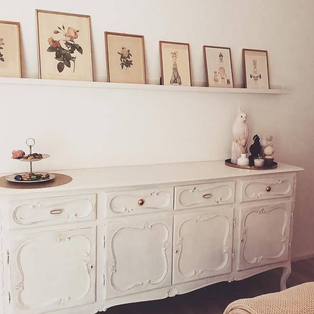 Una cassettiera bianca con quadri sulla parete dietro