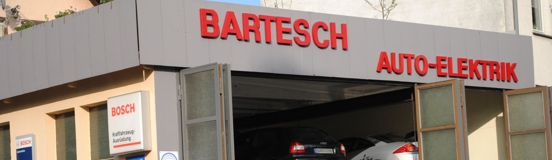 Ein Auto steht in einer Garage unter einem Schild mit der Aufschrift „Bartesch Auto-Elektrik“