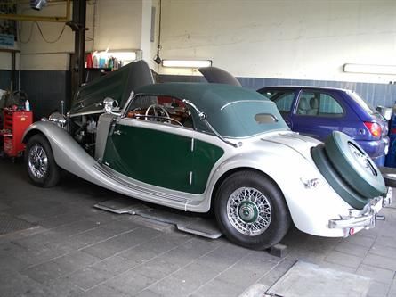 Ein grün-silbernes Auto steht in einer Garage neben einem blauen Auto.