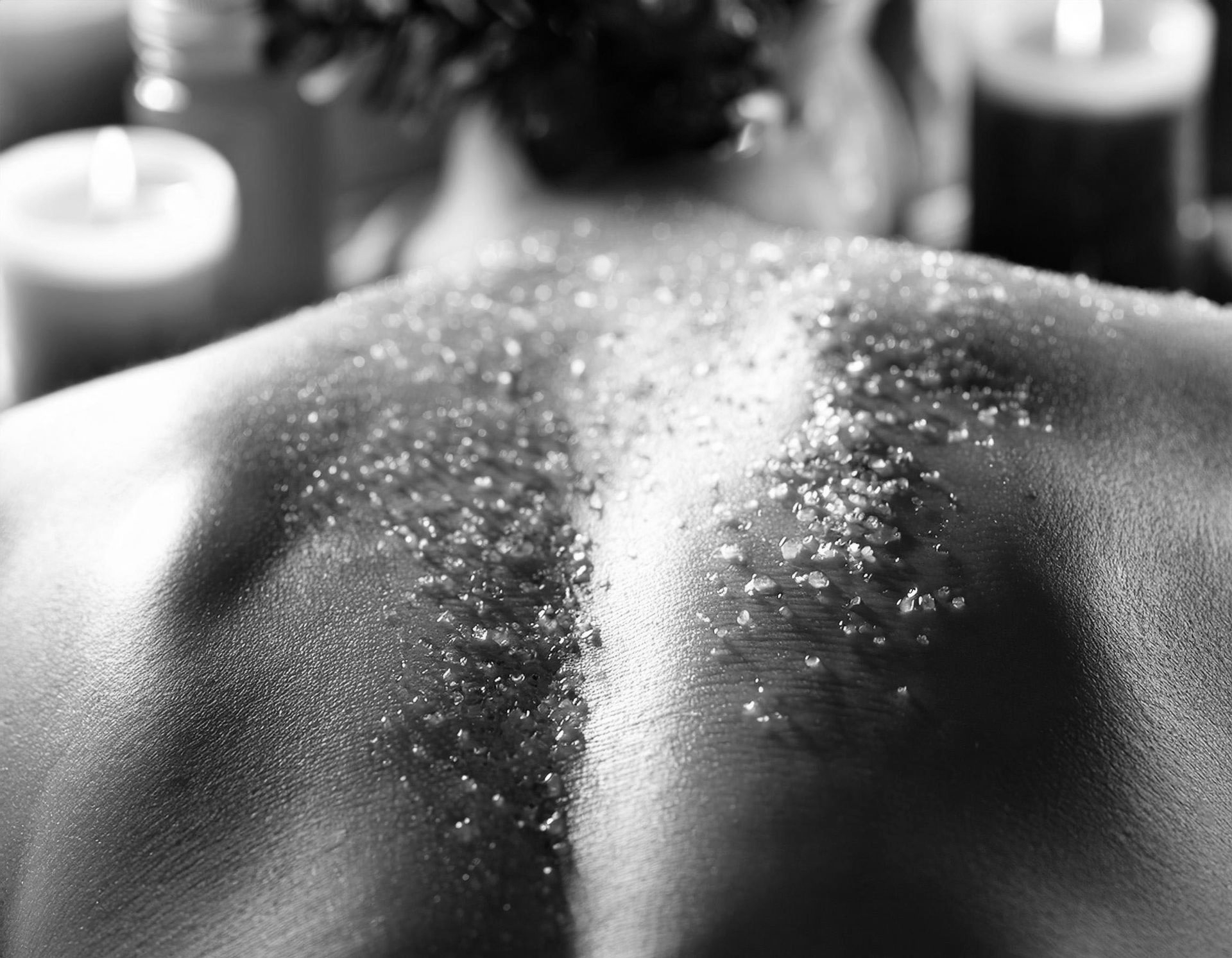 Une personne allongée sur le ventre pendant un soin spa, avec un gommage exfoliant appliqué sur son dos nu.